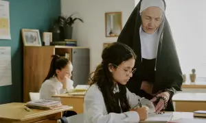 Siostra zakonna pomaga uczennicy w nauce, wskazując na różańcu główne prawdy wiary.