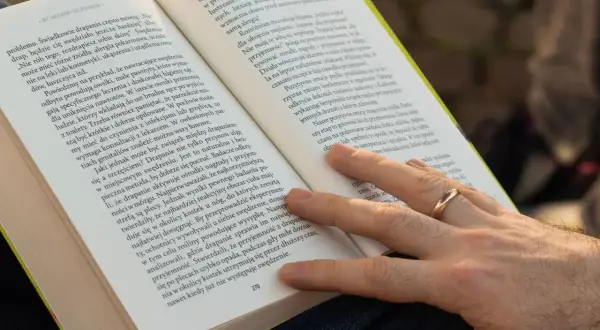 Dłoń z obrączką na palcu, która delikatnie dotyka strony książki. Tekst na stronie opisuje zjawisko wallenrodyzmu i jego wpływ na samopoczucie.