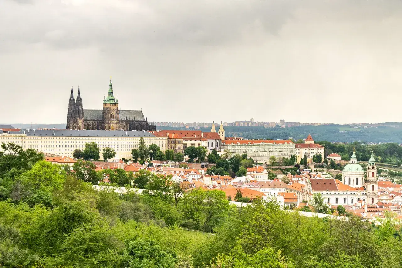 Widok na Zamek Praski i miasto z zielonymi drzewami na pierwszym planie.