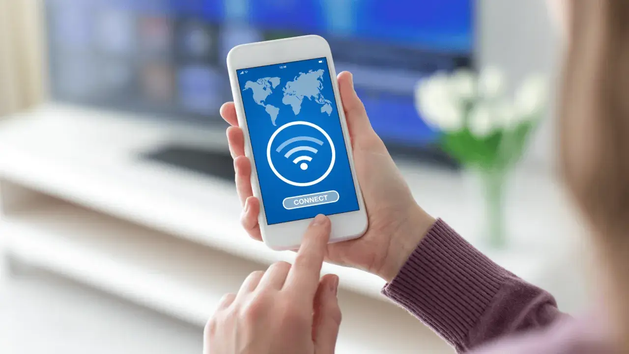 Dłoń trzyma smartfon z mapą świata i ikoną Wi-Fi. Dotyka przycisku "CONNECT", szukając darmowego hotspotu.