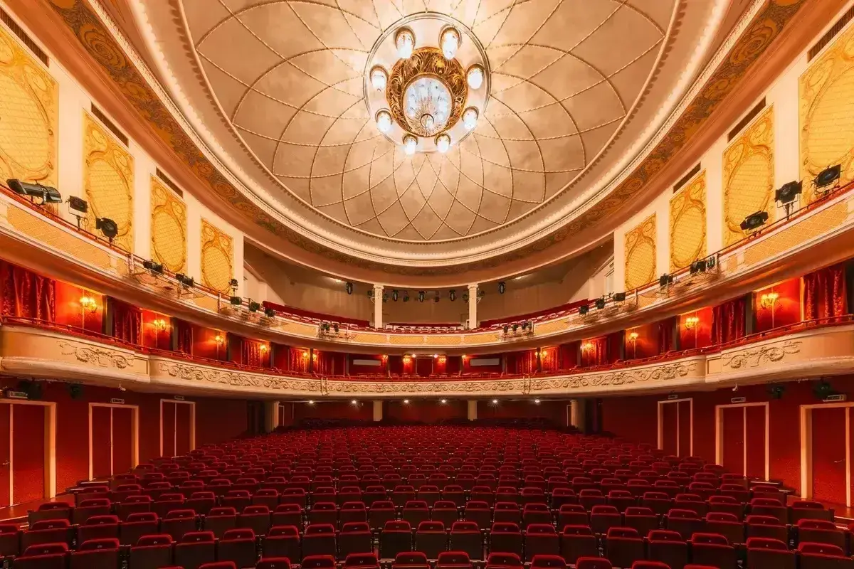 Wnętrze teatru z czerwonymi fotelami i bogato zdobionym sufitem, gotowe na wspaniały performance.