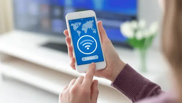 Dłoń trzyma smartfon z mapą świata i ikoną Wi-Fi. Dotyka przycisku "CONNECT", szukając darmowego hotspotu.