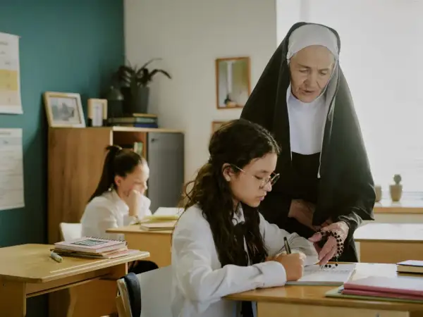 Siostra zakonna pomaga uczennicy w nauce, wskazując na różańcu główne prawdy wiary.