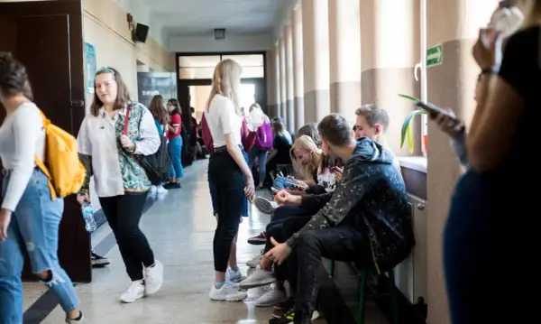 Uczniowie w szkolnym korytarzu, niektórzy siedzą, inni idą. Czy to sigma?